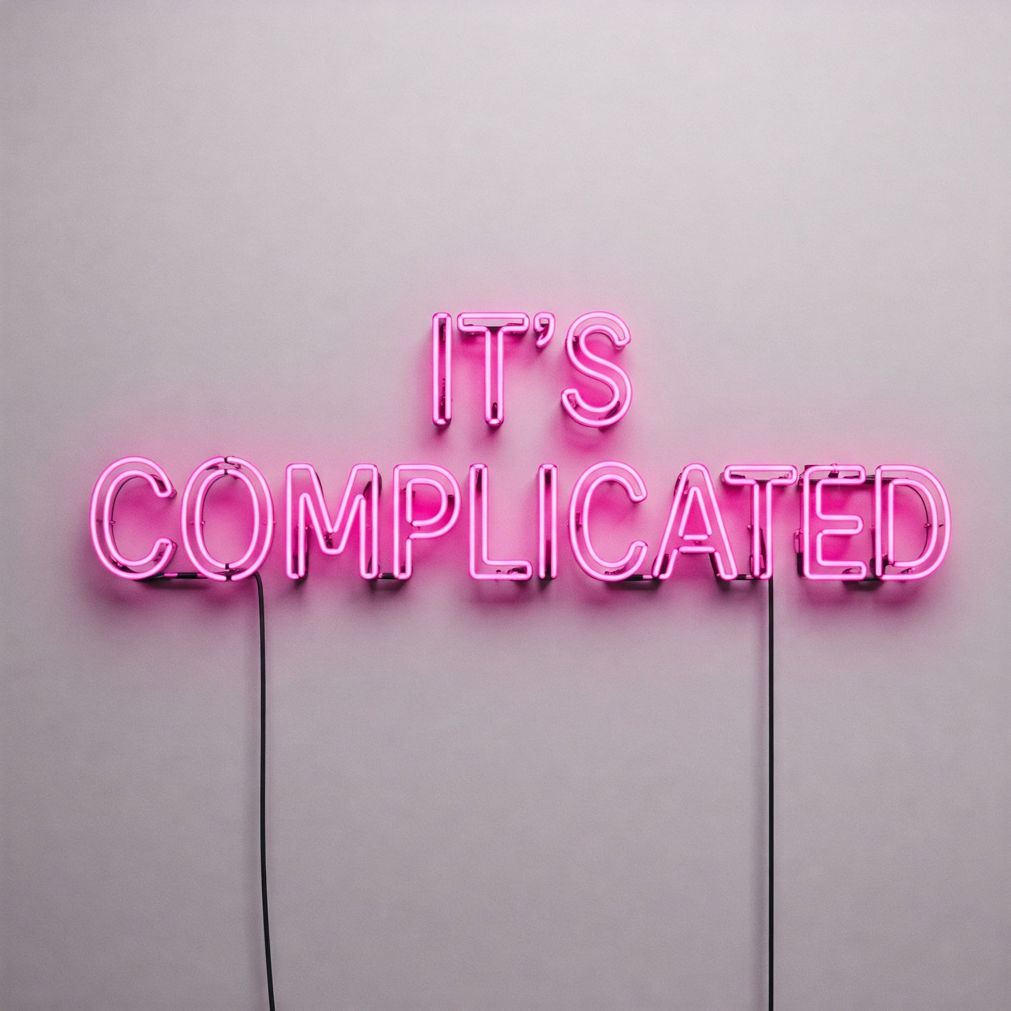 Neon pink sign reading 'IT'S COMPLICATED' on a gray wall, symbolizing complexity in decision-making, relationships, or technology.